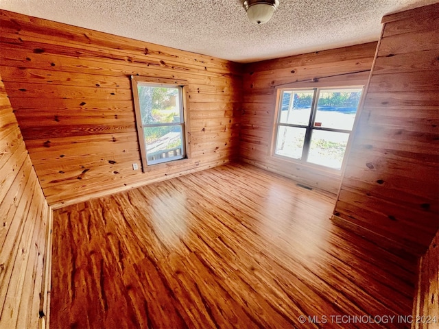 empty room featuring wood walls, a textured ceiling, wood-type flooring, and plenty of natural light