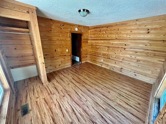 unfurnished bedroom featuring wooden walls, a textured ceiling, visible vents, and light wood-style floors