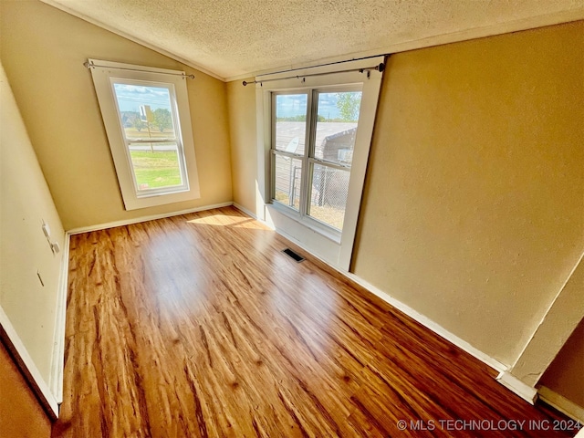 unfurnished room featuring lofted ceiling, a textured ceiling, and hardwood / wood-style flooring