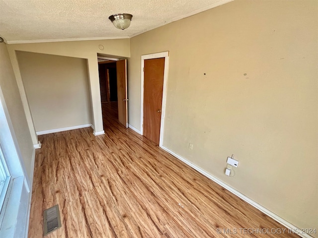 spare room featuring lofted ceiling, a textured ceiling, ornamental molding, and light wood-type flooring