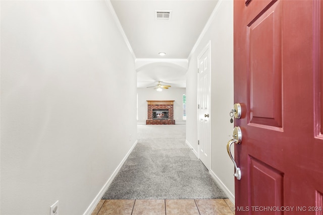 tiled entryway featuring ornamental molding, ceiling fan, and a brick fireplace