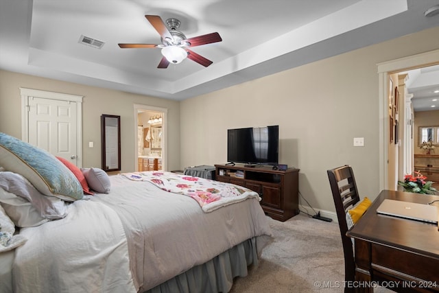 carpeted bedroom featuring a raised ceiling, ensuite bathroom, and ceiling fan