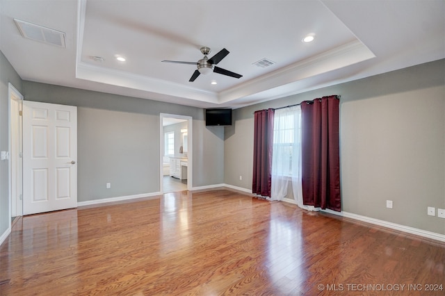 spare room with ornamental molding, ceiling fan, wood-type flooring, and a raised ceiling