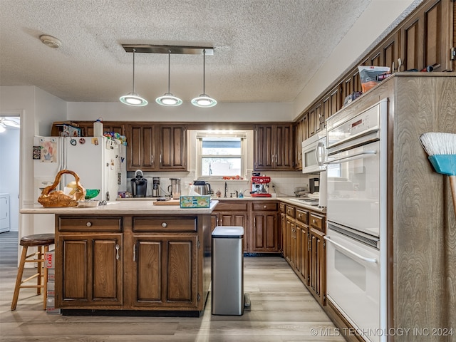 kitchen featuring white appliances, a center island, light hardwood / wood-style floors, pendant lighting, and a breakfast bar