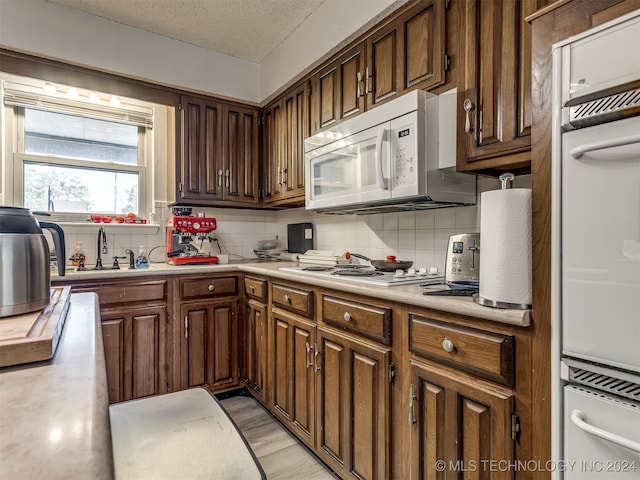 kitchen featuring backsplash, sink, light wood-type flooring, a textured ceiling, and white appliances