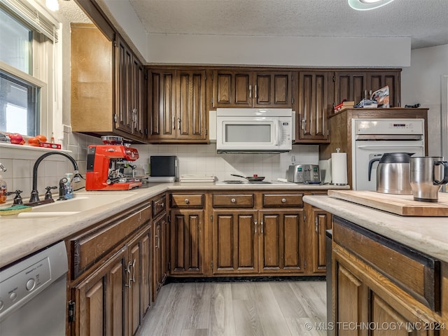 kitchen with white appliances, sink, backsplash, a textured ceiling, and light hardwood / wood-style floors