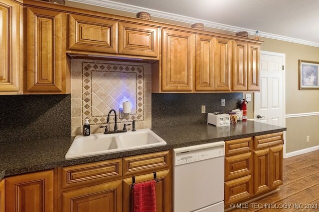 kitchen featuring sink, backsplash, white dishwasher, hardwood / wood-style floors, and crown molding