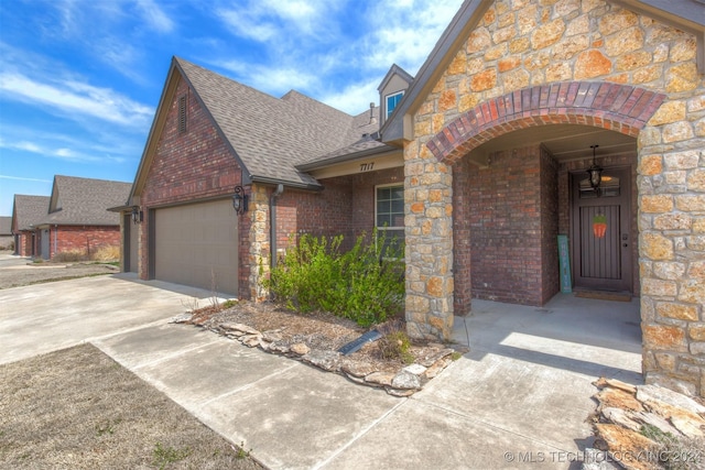 view of front of house with driveway, roof with shingles, brick siding, an attached garage, and stone siding