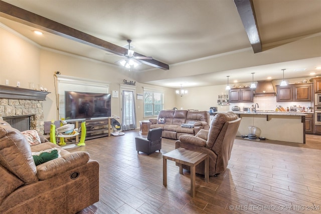 living room with a stone fireplace, ceiling fan with notable chandelier, wood finished floors, beamed ceiling, and ornamental molding