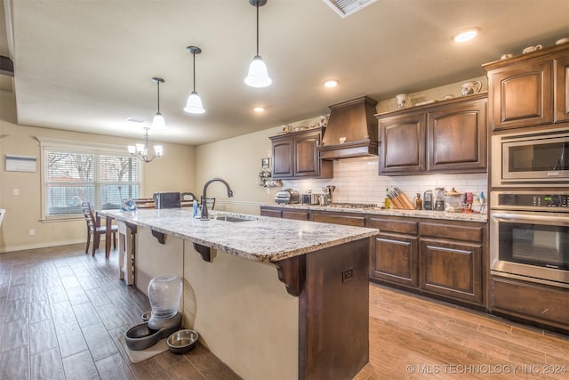 kitchen with light stone counters, a kitchen breakfast bar, custom range hood, a sink, and appliances with stainless steel finishes