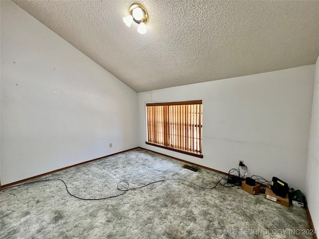 empty room featuring a textured ceiling, carpet flooring, and vaulted ceiling