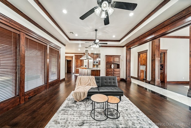 living room with dark wood-type flooring, crown molding, a raised ceiling, and ceiling fan