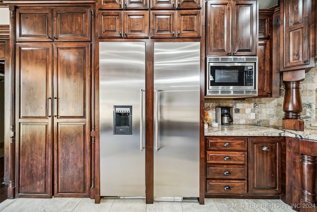 kitchen featuring tasteful backsplash, appliances with stainless steel finishes, dark brown cabinetry, light stone counters, and light tile patterned floors