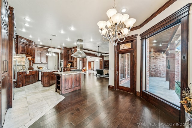 kitchen with ceiling fan with notable chandelier, island range hood, pendant lighting, hardwood / wood-style flooring, and a center island with sink