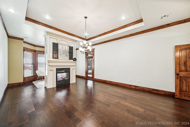 unfurnished living room with a large fireplace, a tray ceiling, dark wood-type flooring, crown molding, and a notable chandelier