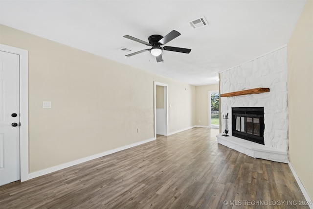 unfurnished living room featuring a stone fireplace, dark wood-type flooring, and ceiling fan