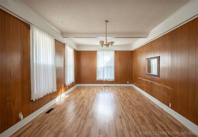 empty room featuring wood walls, hardwood / wood-style floors, a notable chandelier, and a textured ceiling