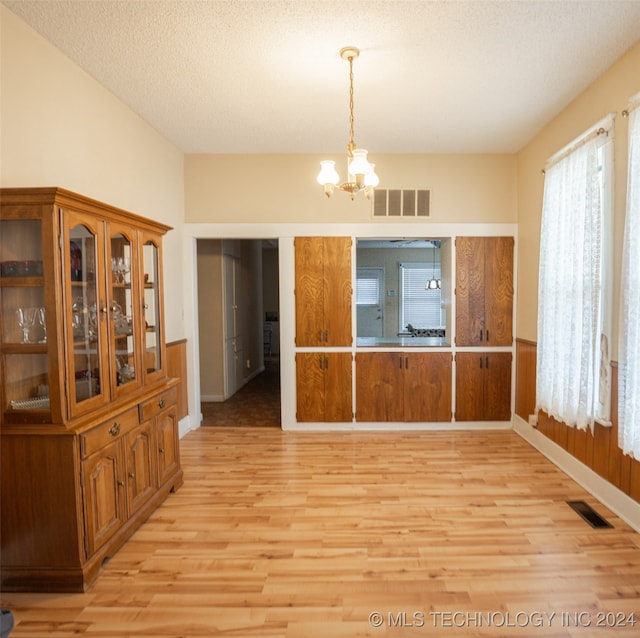 unfurnished dining area with light wood-type flooring, a chandelier, and a textured ceiling