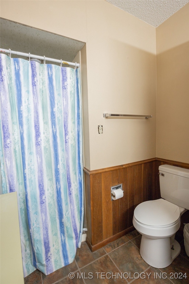 bathroom featuring walk in shower, a textured ceiling, wooden walls, tile patterned floors, and toilet