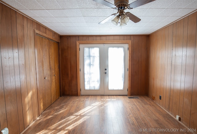 spare room with wood walls, ceiling fan, wood-type flooring, and french doors