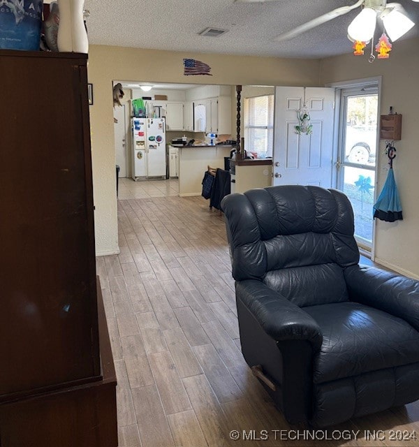 living room featuring light hardwood / wood-style flooring, a textured ceiling, and ceiling fan