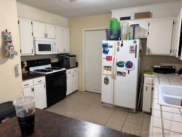 kitchen with white appliances, tile countertops, a textured ceiling, white cabinetry, and light tile patterned floors