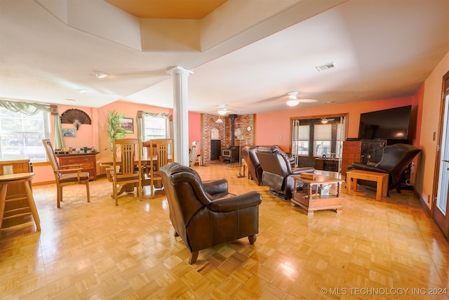 living room featuring ornate columns, a wood stove, and a wealth of natural light