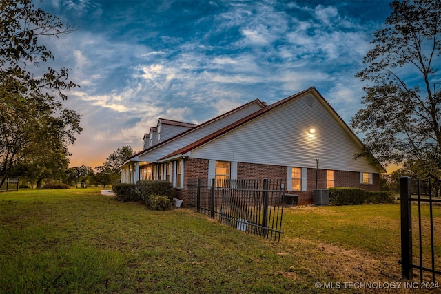 property exterior at dusk with central AC and a lawn