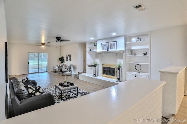 living room with a brick fireplace, light wood-type flooring, and ceiling fan