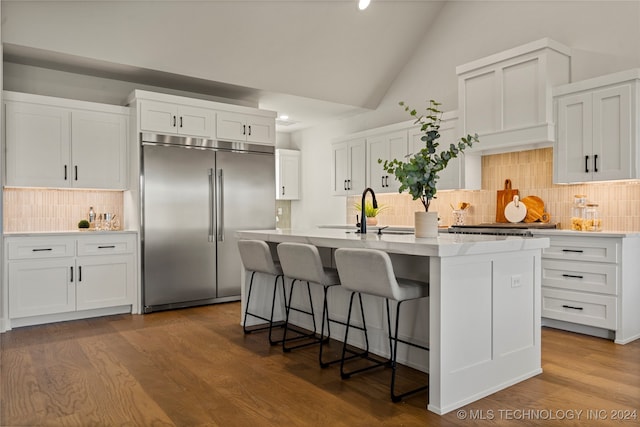 kitchen featuring white cabinets, hardwood / wood-style floors, built in fridge, and an island with sink