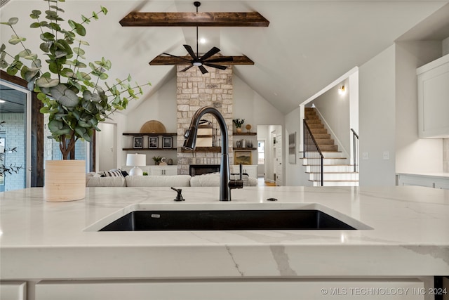 kitchen with vaulted ceiling with beams, sink, light stone counters, and a fireplace