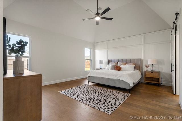 bedroom with hardwood / wood-style floors, a barn door, high vaulted ceiling, and ceiling fan