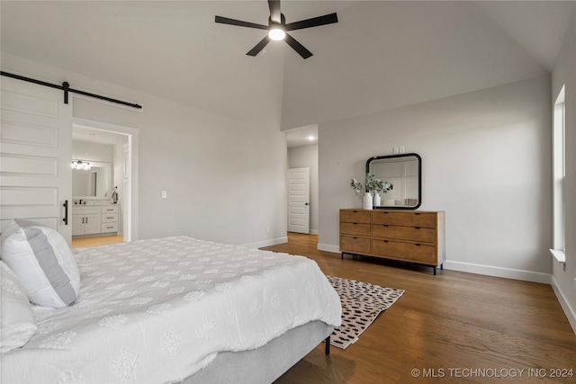 bedroom with ceiling fan, a barn door, hardwood / wood-style flooring, high vaulted ceiling, and ensuite bath