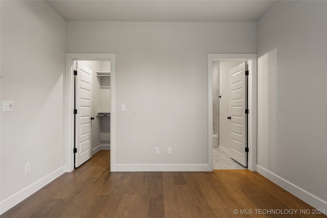 unfurnished bedroom with a closet, connected bathroom, a spacious closet, and wood-type flooring