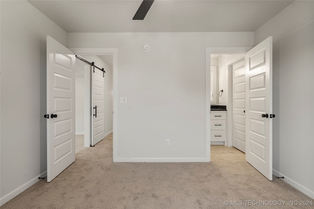 unfurnished bedroom with light colored carpet, ceiling fan, and a barn door