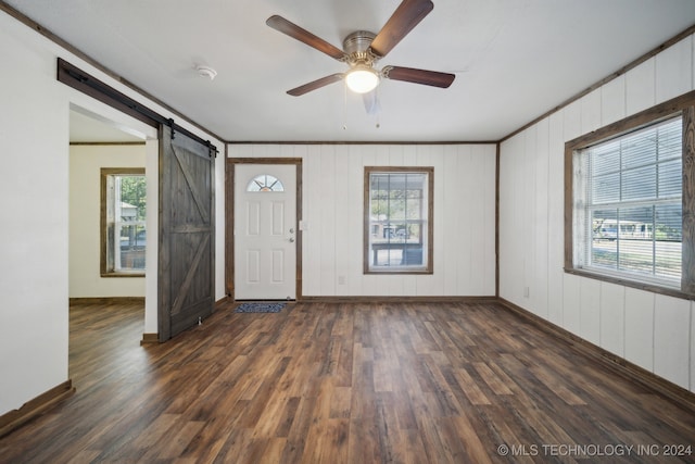 entrance foyer with wood walls, a barn door, dark hardwood / wood-style flooring, ceiling fan, and ornamental molding