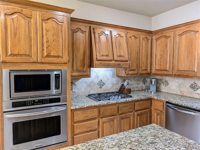 kitchen with light stone countertops, appliances with stainless steel finishes, and tasteful backsplash