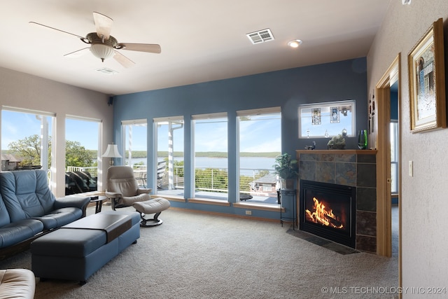 carpeted living room with a water view, ceiling fan, and a tile fireplace