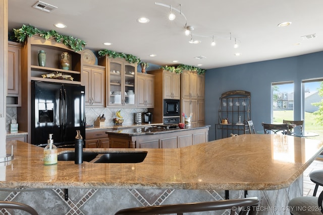 kitchen with a spacious island, black appliances, decorative backsplash, and a kitchen bar