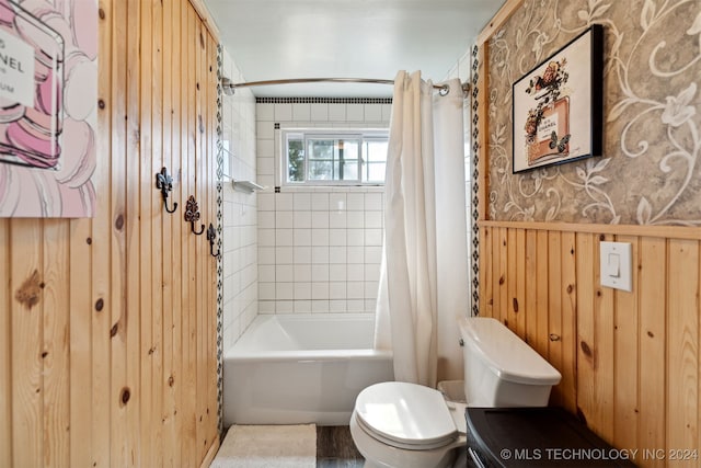 bathroom featuring toilet, shower / bath combo with shower curtain, and wooden walls