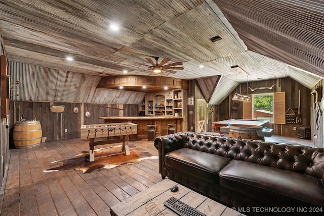 recreation room with wood walls, wood-type flooring, bar area, ceiling fan, and vaulted ceiling