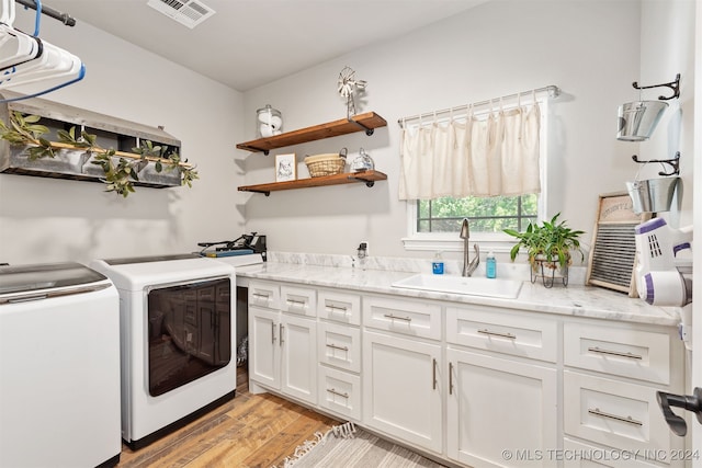 laundry room with light hardwood / wood-style flooring, independent washer and dryer, sink, and cabinets