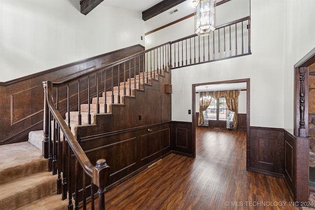 stairway featuring beam ceiling, hardwood / wood-style floors, a notable chandelier, and a towering ceiling