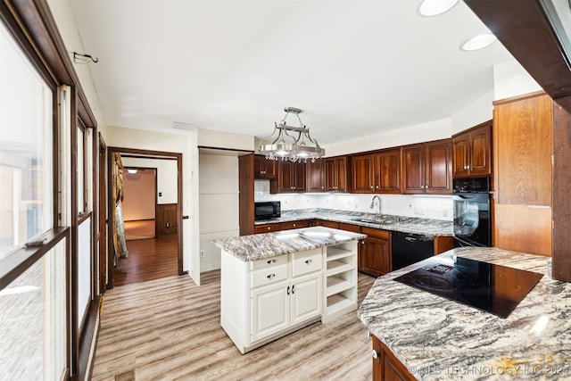 kitchen with black appliances, light wood-type flooring, a kitchen island, decorative light fixtures, and light stone counters