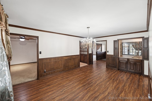 unfurnished dining area featuring ornamental molding, dark hardwood / wood-style floors, wooden walls, and ceiling fan with notable chandelier