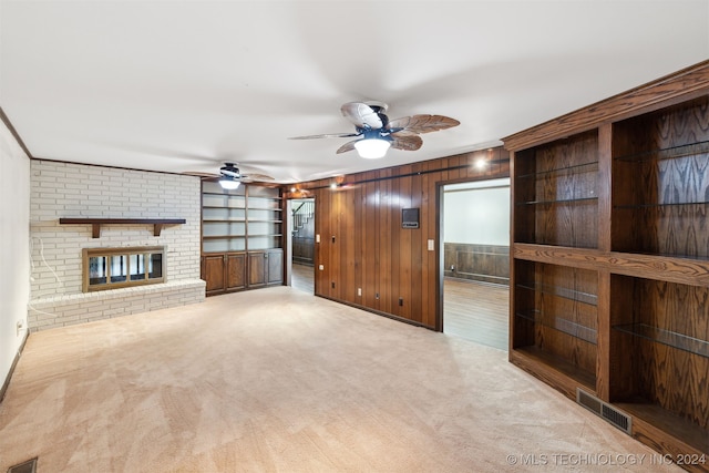 unfurnished living room featuring wood walls, a brick fireplace, light carpet, ornamental molding, and built in shelves