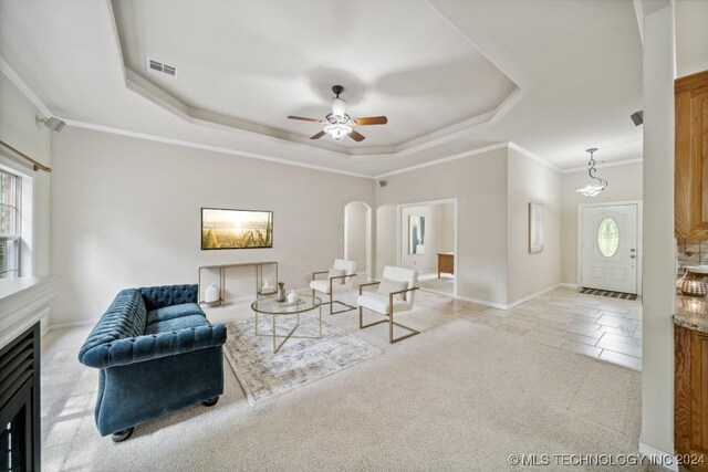 living room featuring a fireplace, a tray ceiling, light carpet, ceiling fan, and ornamental molding