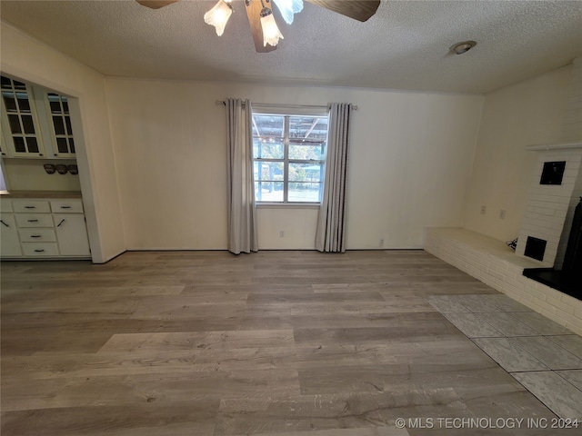 unfurnished living room featuring light hardwood / wood-style floors, a textured ceiling, a fireplace, and ceiling fan