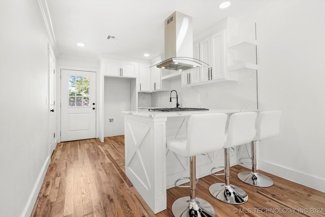 kitchen with a kitchen bar, island exhaust hood, white cabinetry, ornamental molding, and light hardwood / wood-style flooring