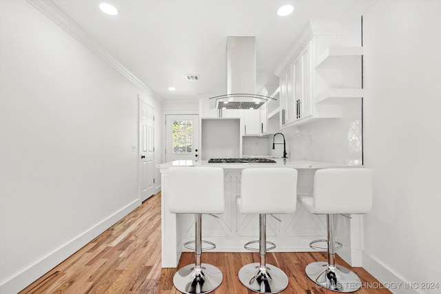 kitchen featuring island range hood, a kitchen breakfast bar, kitchen peninsula, light wood-type flooring, and white cabinets